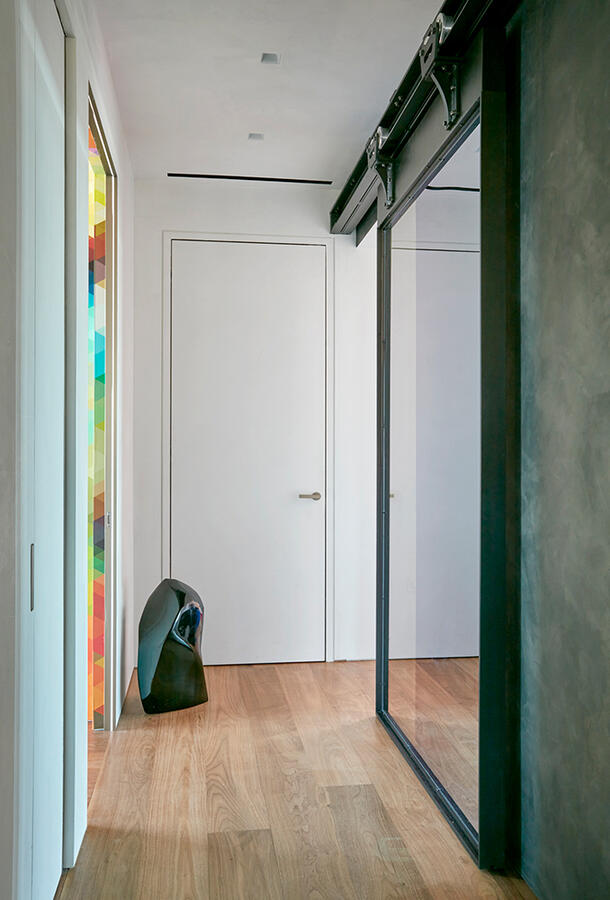 Hallway of an apartment with a thick sliding door to the right and an abstract stone-shaped sculpture in the left corner