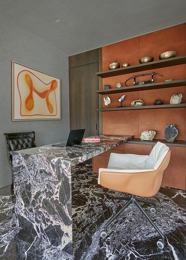 A home office with a grey and orange accented wall. The floor and office desk are made of dark marble with two chairs on each side.